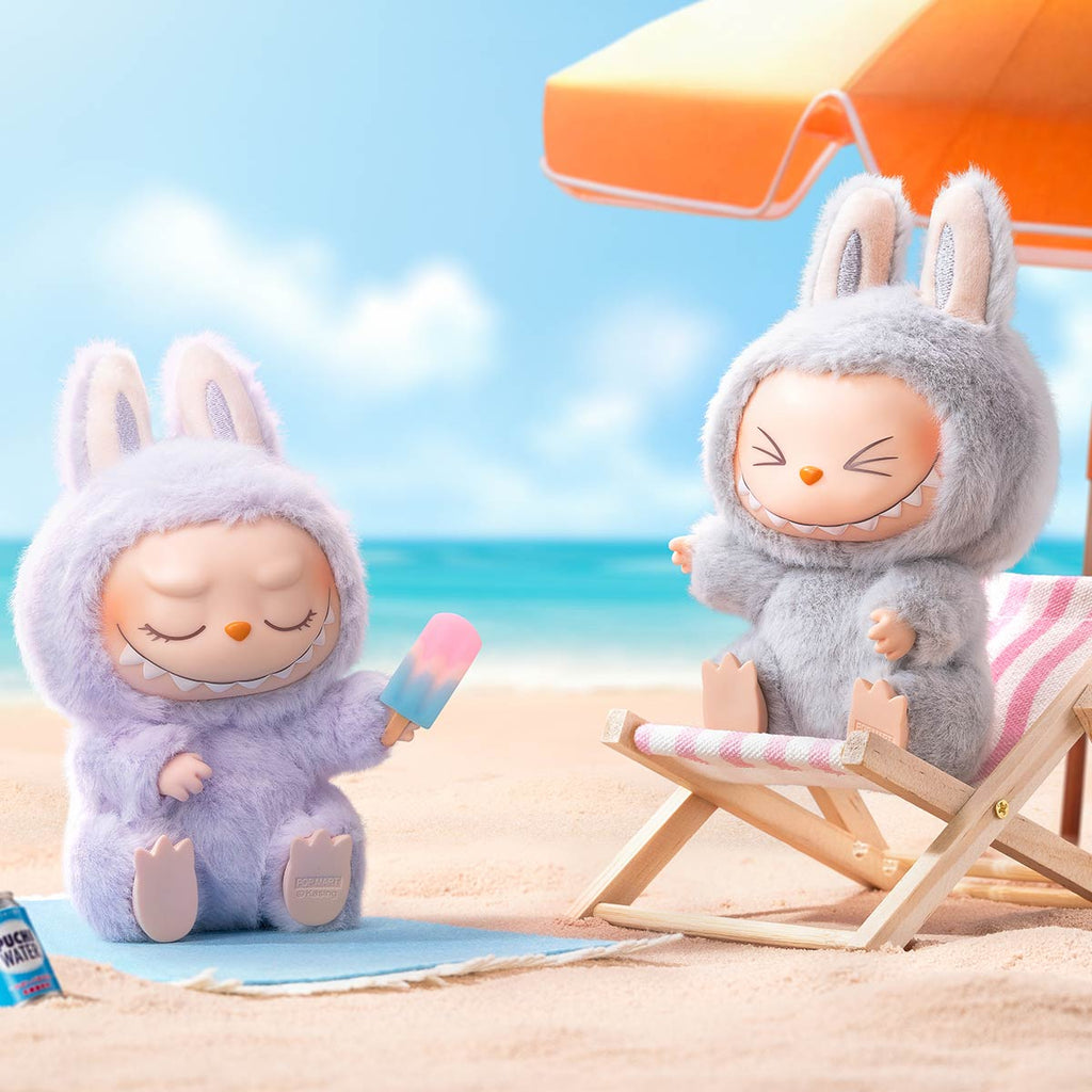 Two Pop Mart Labubu costumes on a beach with an umbrella and ocean view.