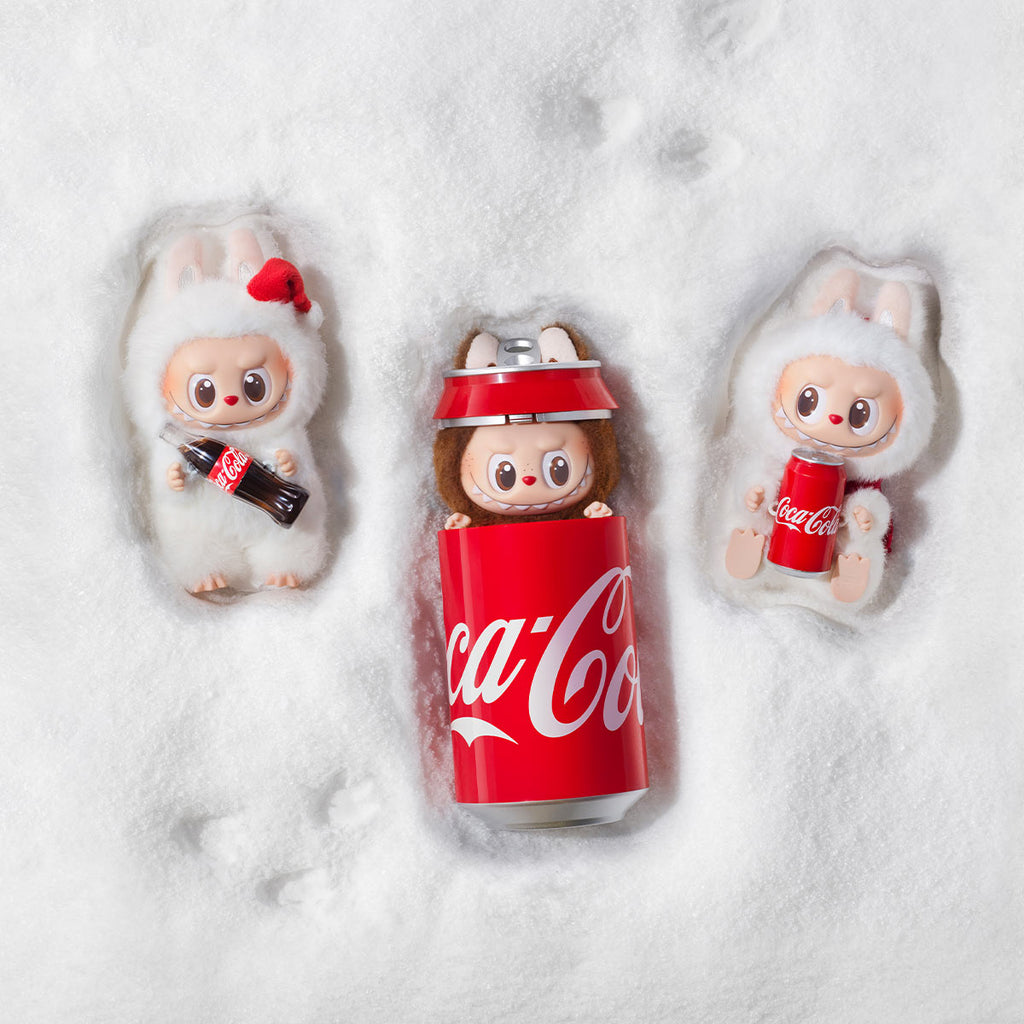 Three small Pop Mart Labubu inside Coca-Cola cans on a snowy background