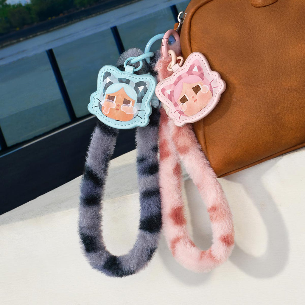 Two Pop Mart Labubu keychains with cartoon faces attached to a brown bag by a body of water.
