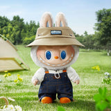 Plush POP MART Labubu wearing a hat and overalls in a grassy outdoor setting with a tent and flowers.