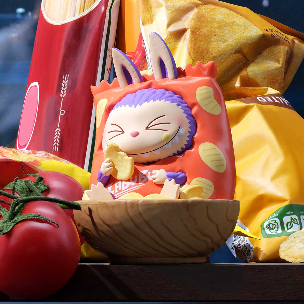 Pop Mart Labubu in a red outfit with bunny ears sitting in a wooden bowl surrounded by snacks and a tomato.