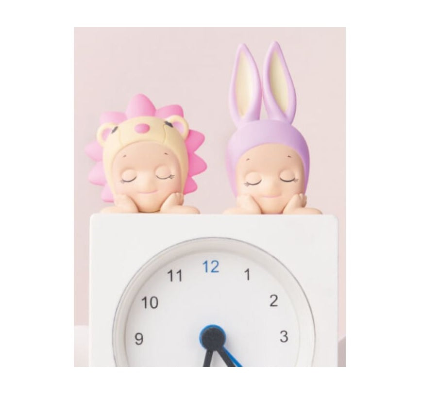 Two Sonny Angel Hipper Dreaming Series with colorful hair on top of a clock against a light pink background