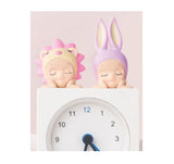 Two Sonny Angel Hipper Dreaming Series with colorful hair on top of a clock against a light pink background