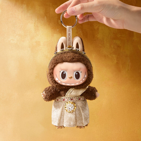 POP MART Good luck to you keychain of a character in a costume held by a hand against a yellow background
