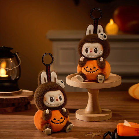 POP MART Hirono Sitting Pumpkin Plush toys in Halloween costumes on a wooden surface with a warm background.