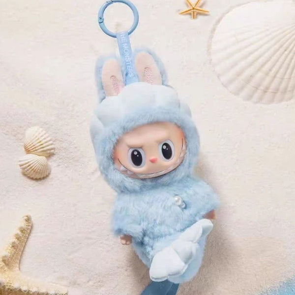 Labubu in a blue bunny costume on a textured beige background with shells.