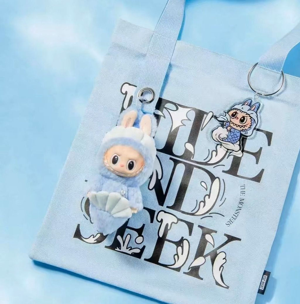 Blue Labubu plush toy with a shell on a tote bag with text and graphics.